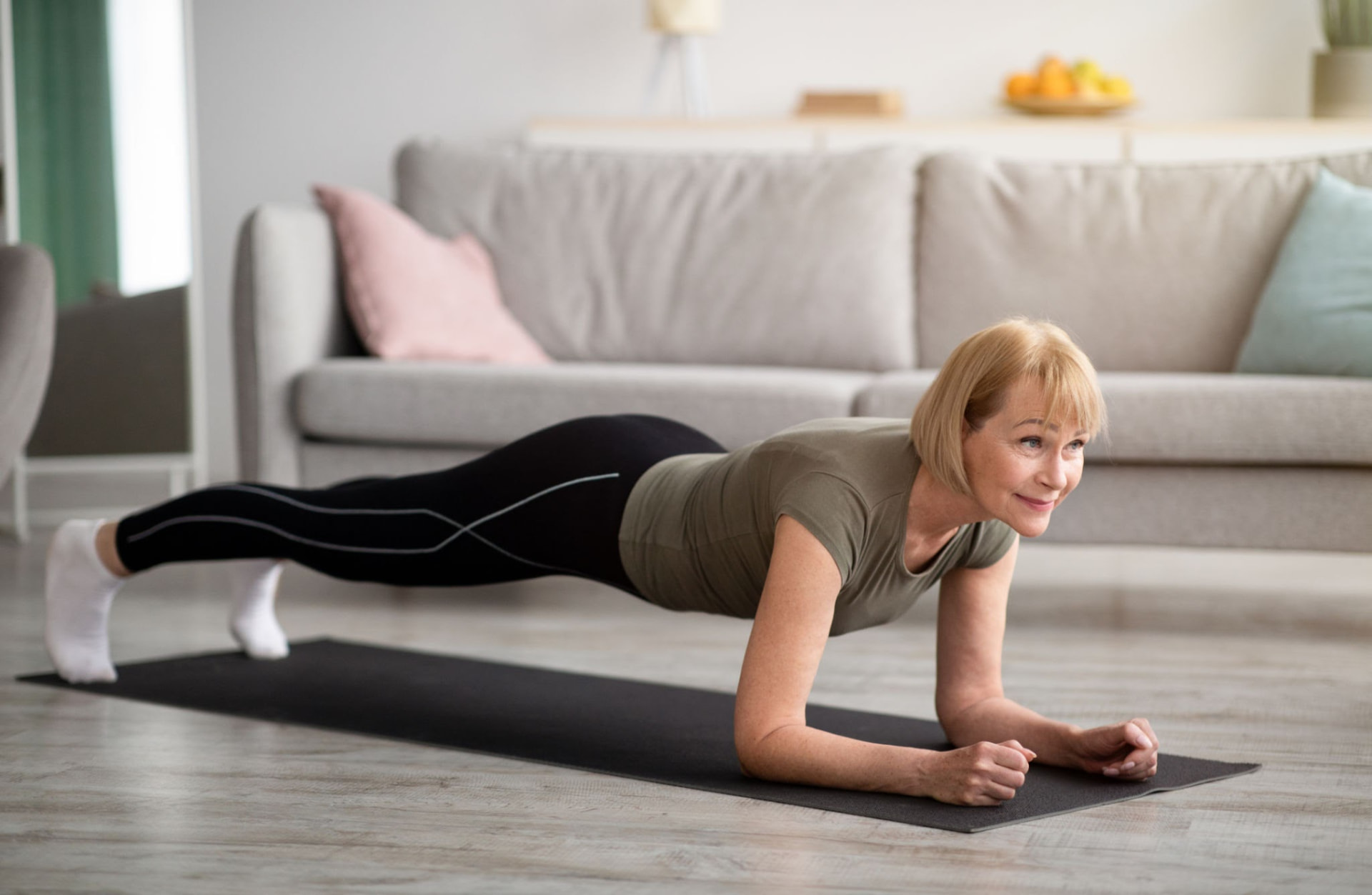Older woman holding a forearm plank on a mat in her living room